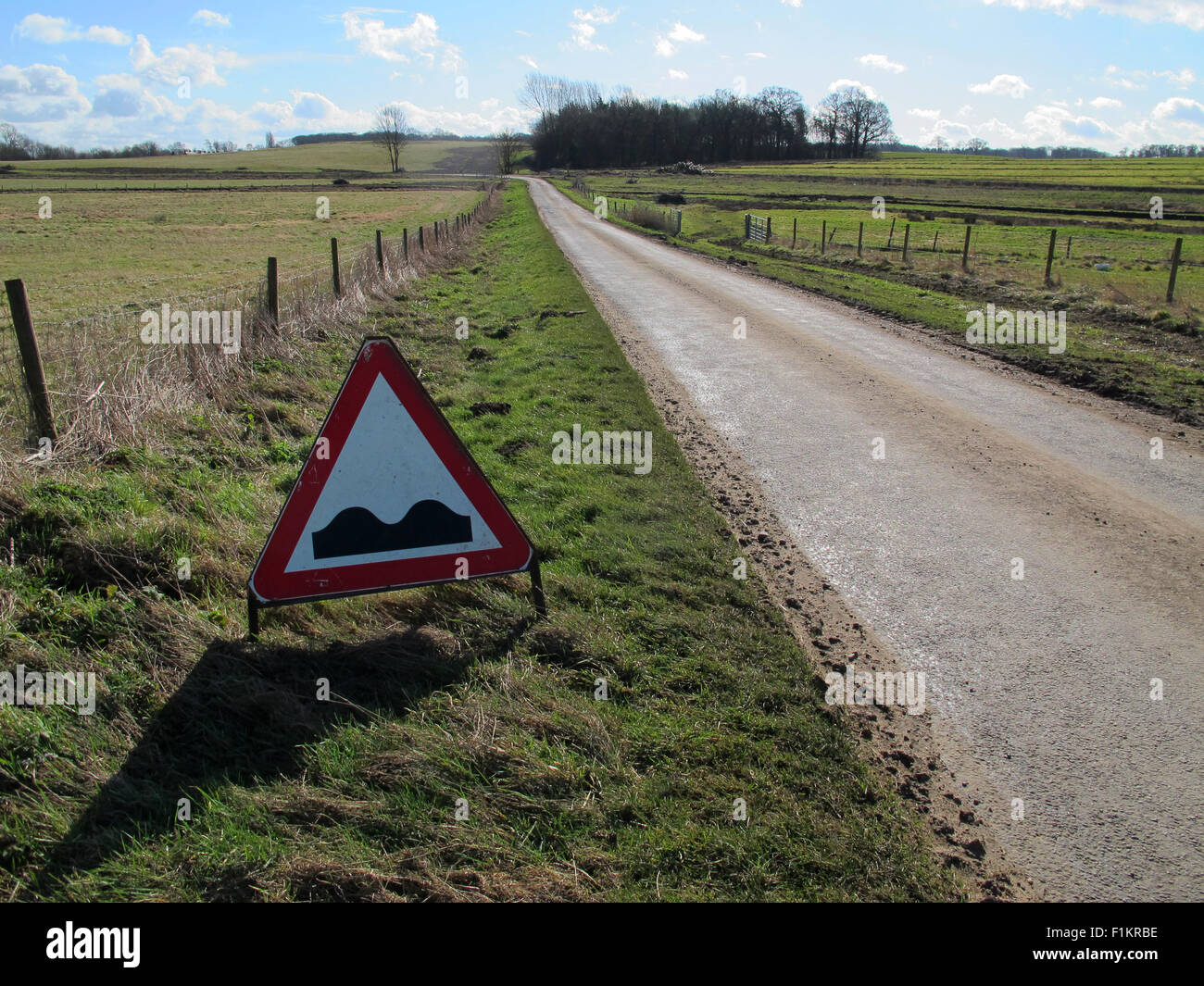 Green grass verges fences country roads have a tendency to be uneven, road warning sign in a red warning triangle two bumps. Stock Photo