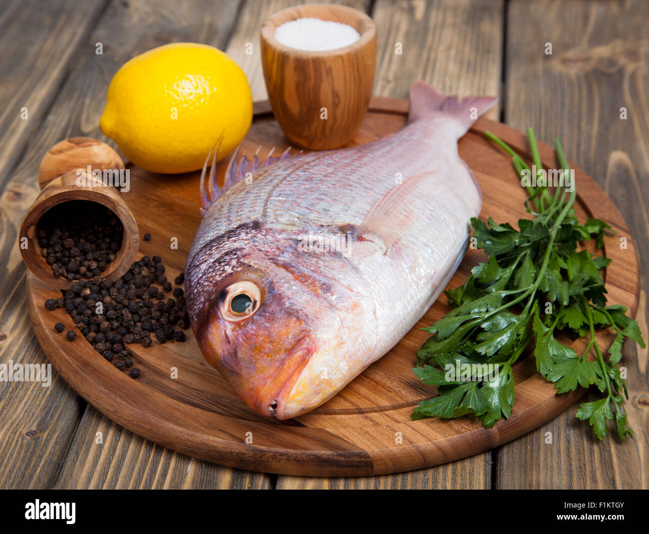 Fresh fish Pagr on a wooden board with lemon and spices Stock Photo