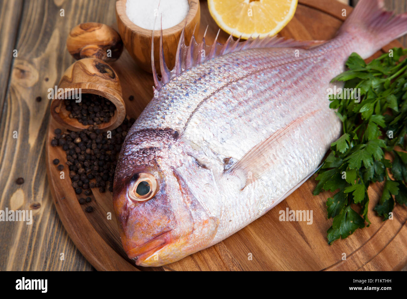 Fresh fish Pagr on a wooden board with lemon and spices Stock Photo