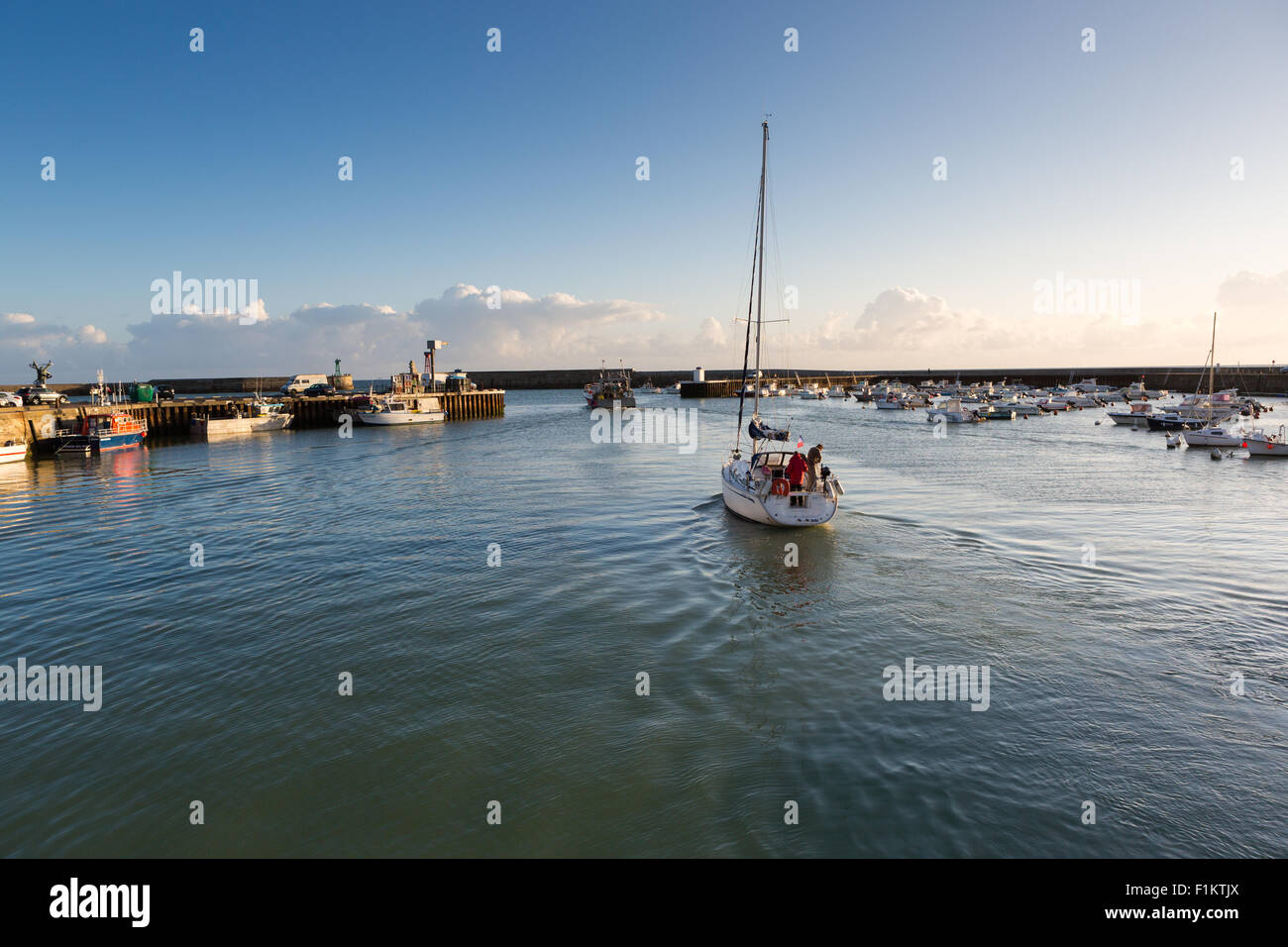 A sailing boat heads out of the harbour at Port-en-Bessin, Calvados ...