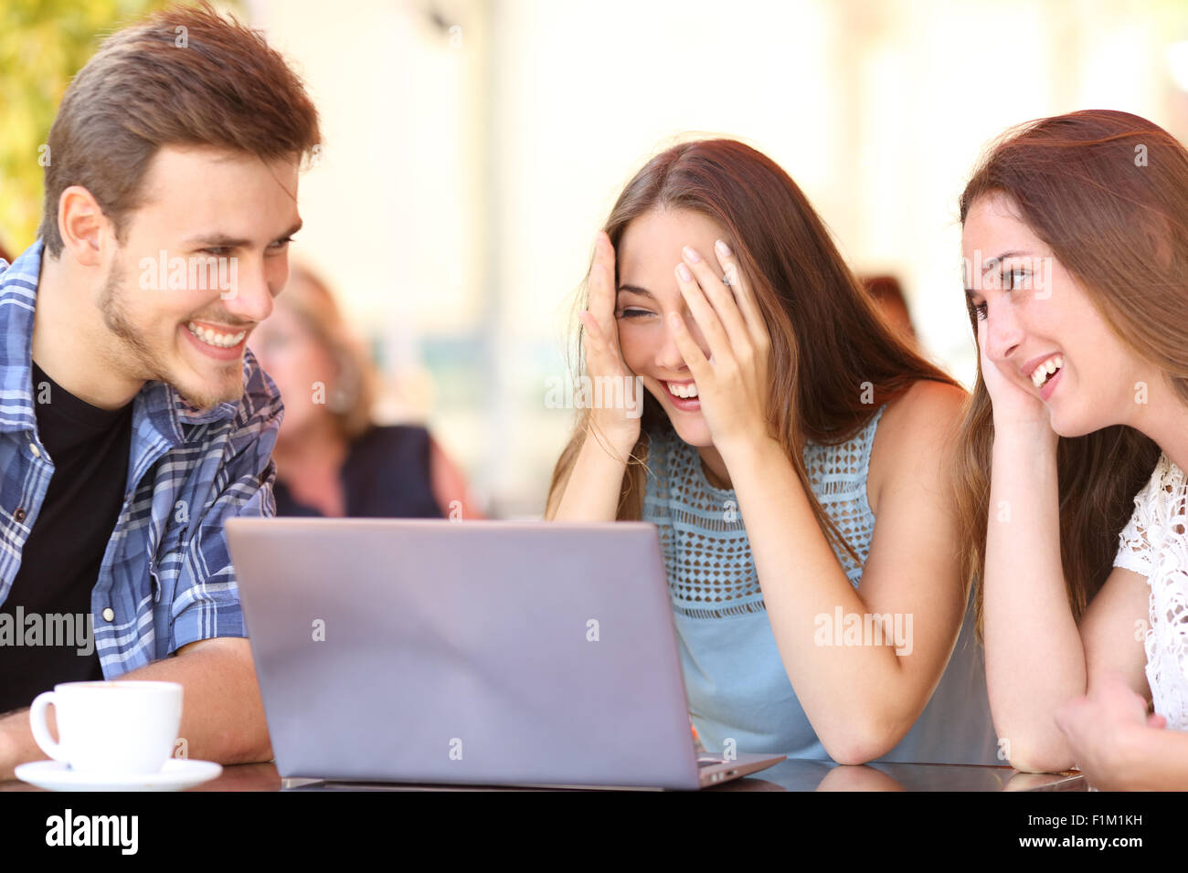 Happy friends giving a laptop gift to a surprised girl in a coffee shop Stock Photo