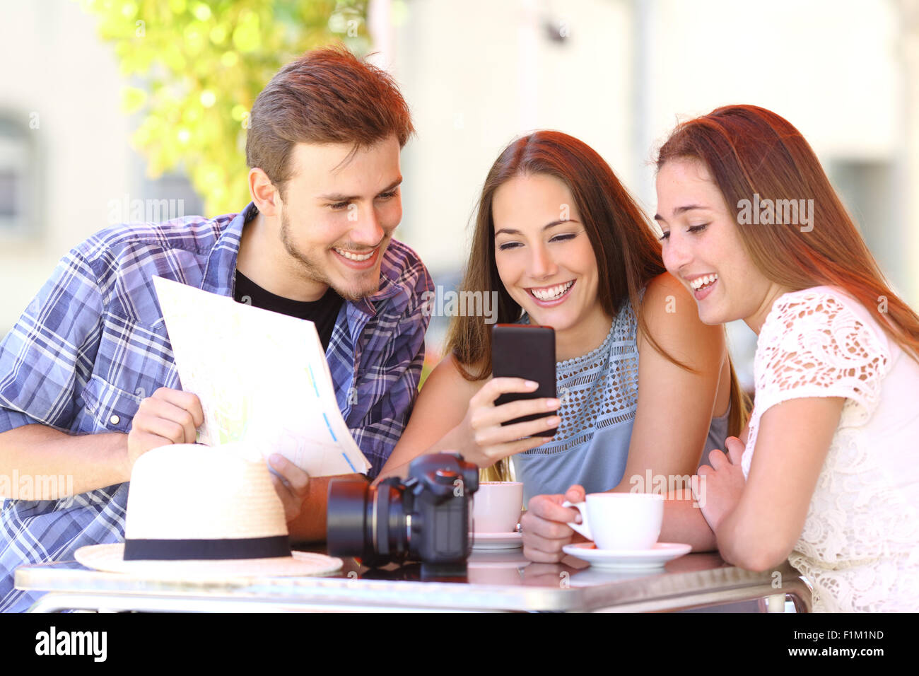 Group of three tourist friends planning vacation with a gps phone and a map in a coffee shop Stock Photo