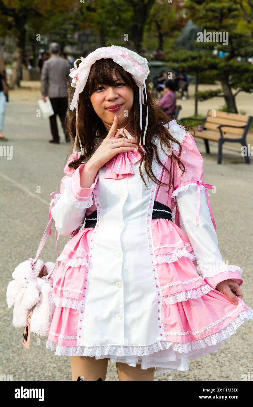 Young Japanese women in Osaka Park dressed in Goth-lolita pink and white maid costume, black kitten socks, posing for viewer. Eye-contact. Stock Photo