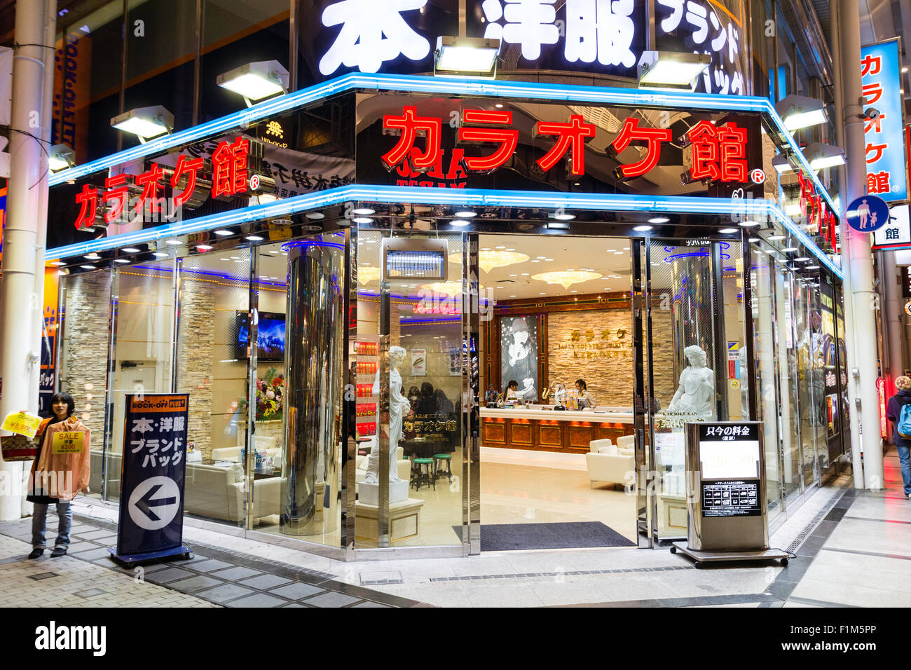 Japan, Osaka. Dotonbori. Glass exterior of Karaoke kan store at night, illuminated, inside two female stafgf members at counter. Stock Photo