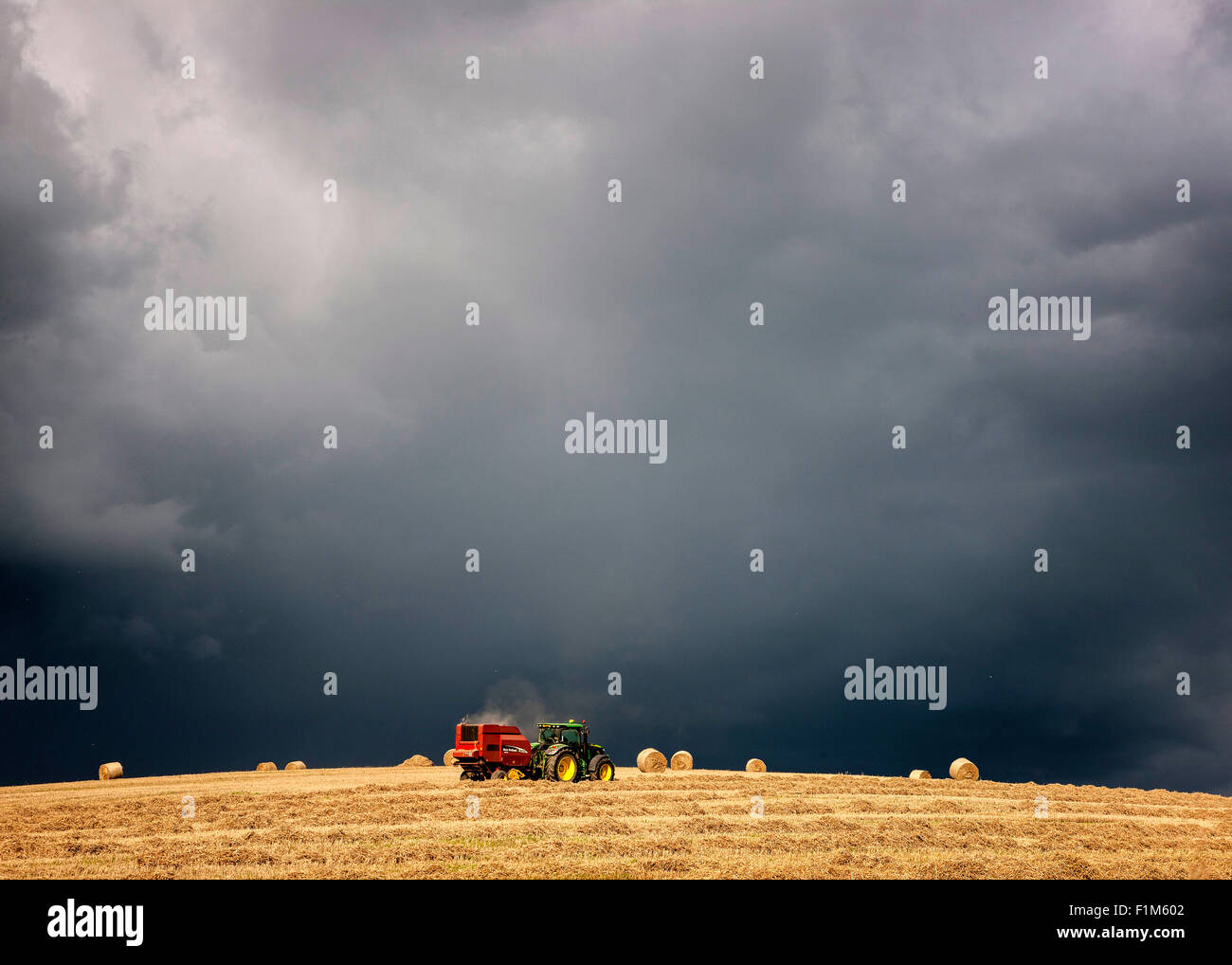 A tractor collecting hay bales under dark black stormy sky Stock Photo ...