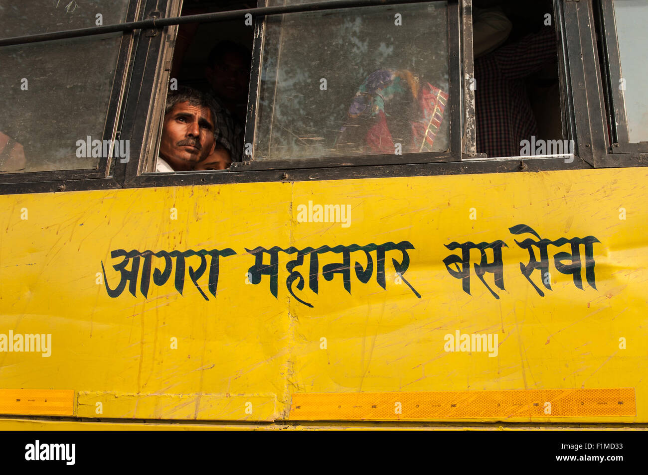 Agra, Utar Pradesh, India. People looking out of a yellow Agra bus with 'Agra Metropolitan Bus Service' written in Hindi. Stock Photo