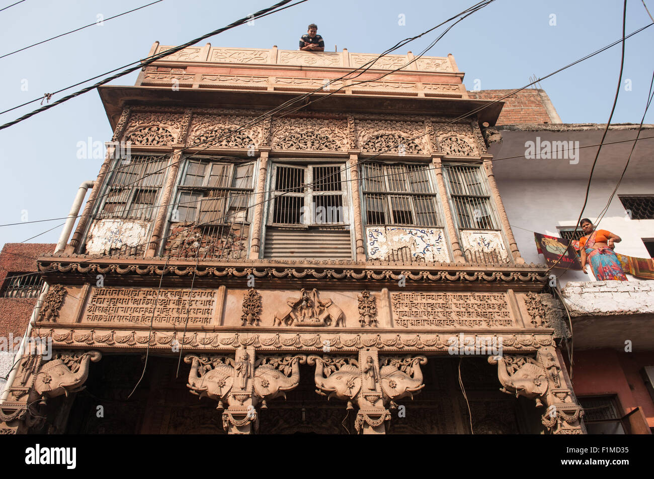 Agra, Uttar Pradesh, India. Richly carved but dilapidated temple to Lakshmi, the goddess of wealth. Elephant carvings and woman on house next door, man on roof. Stock Photo