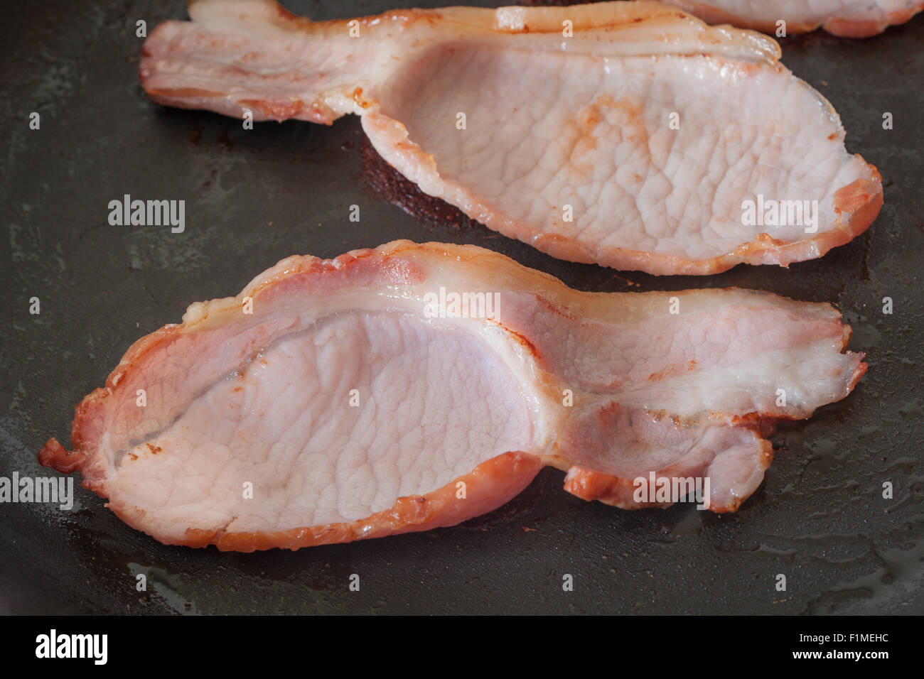Back or middle bacon frying in a pan a traditional cut from the loin and belly Stock Photo