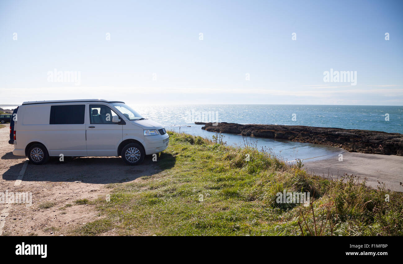 A white VW T5 Camper van parked on clifftop at Porth Ysgaden, Tudweiliog, Llyn Peninsula, North Wales with view across the cove Stock Photo