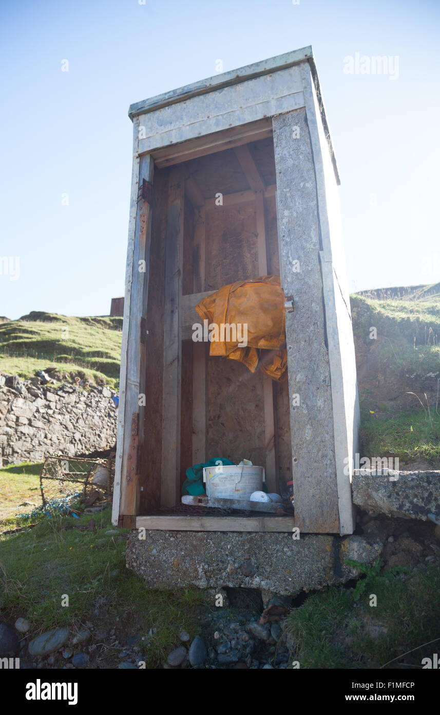 Abandoned fishing hut at Porth Ysgaden, Tudweiliog, Llyn Peninsula, North Wales with yellow storm coat and plastic tubs Stock Photo