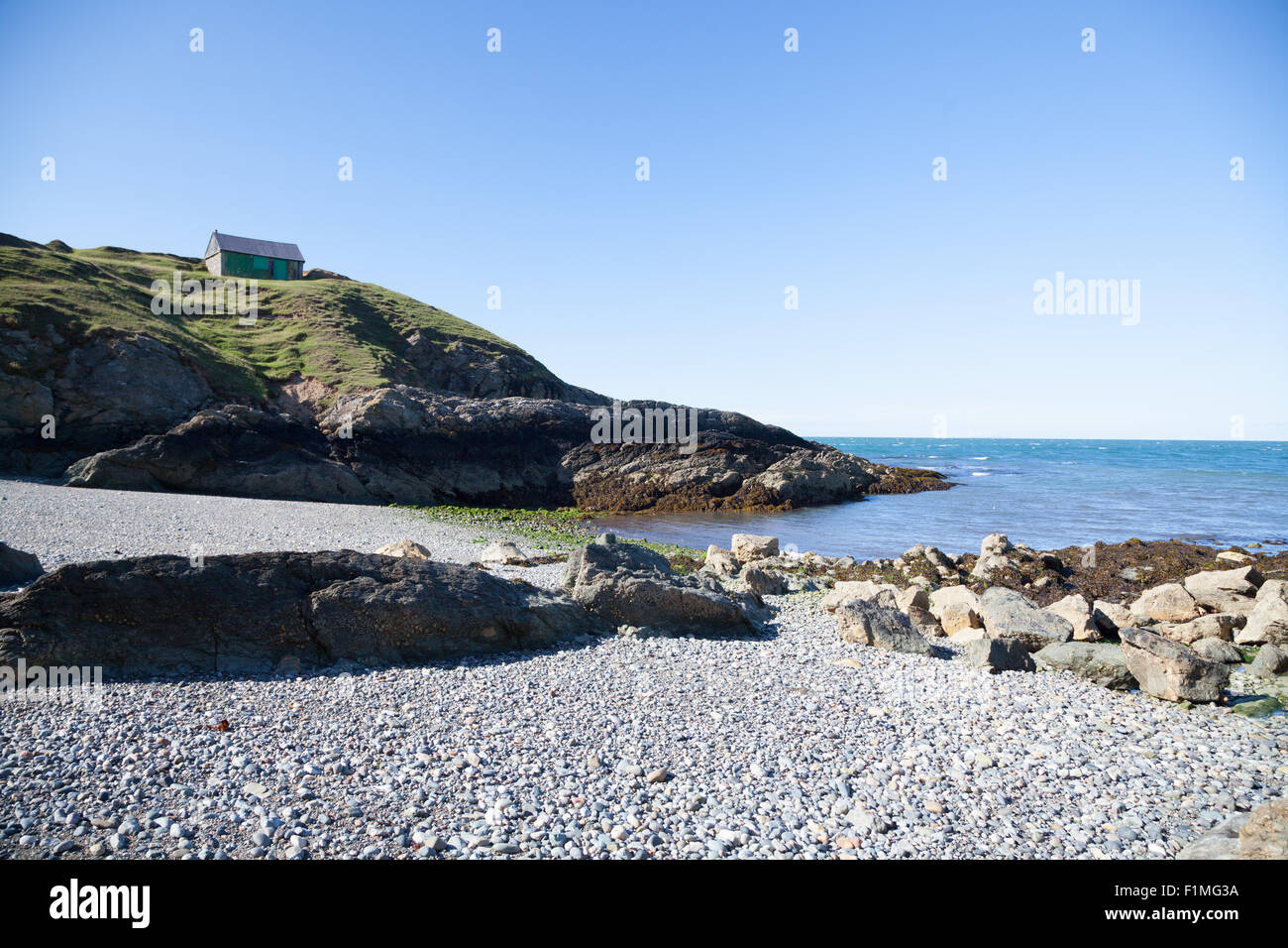 A view across pebble beach at Porth Ysgaden, Tudweiliog, Llyn Peninsula, North Wales with abandoned fishing hut on clifftop Stock Photo