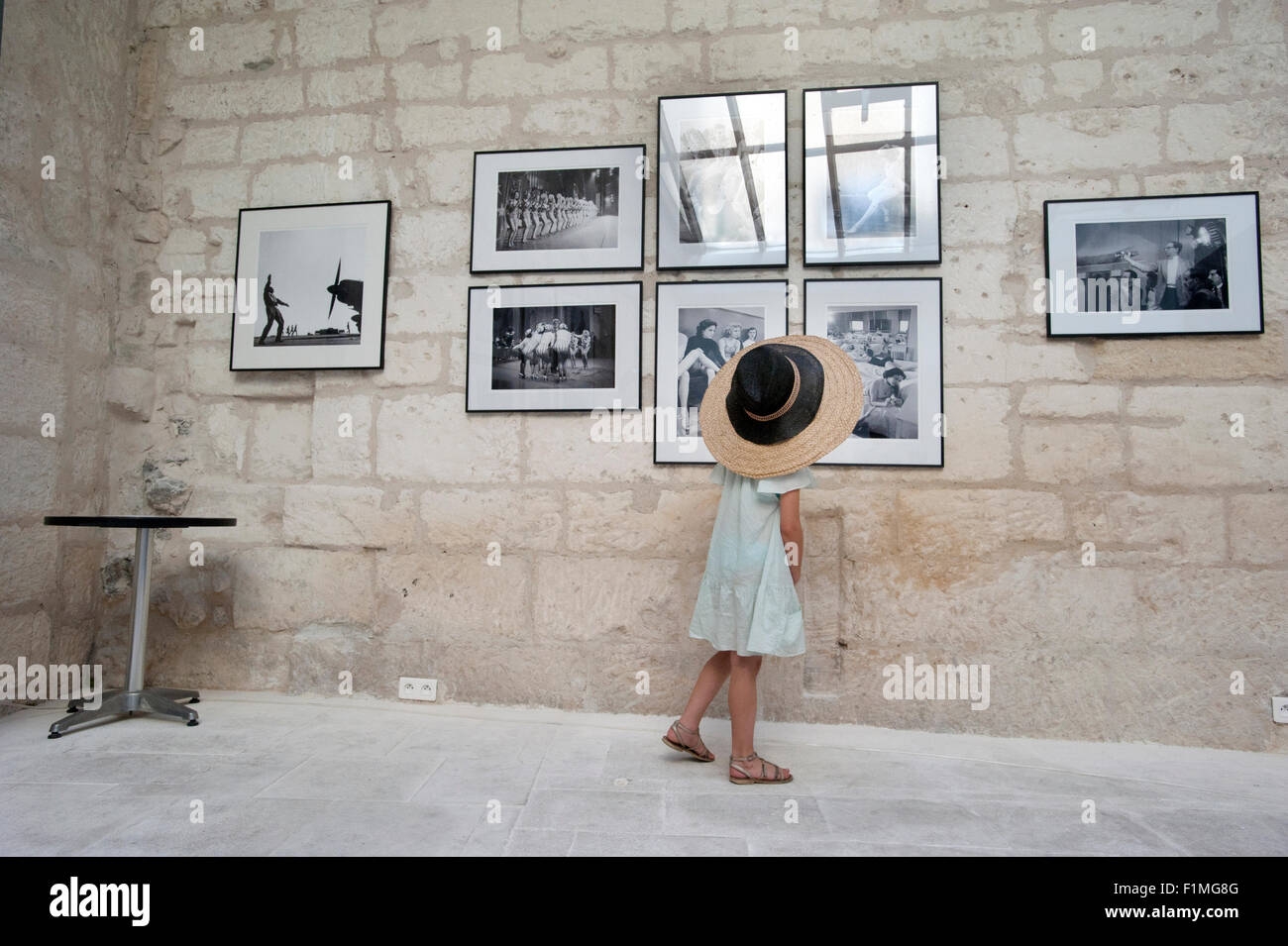 A small girl wearing two hats looks at vintage photographs in an art gallery in Arles, France. Stock Photo
