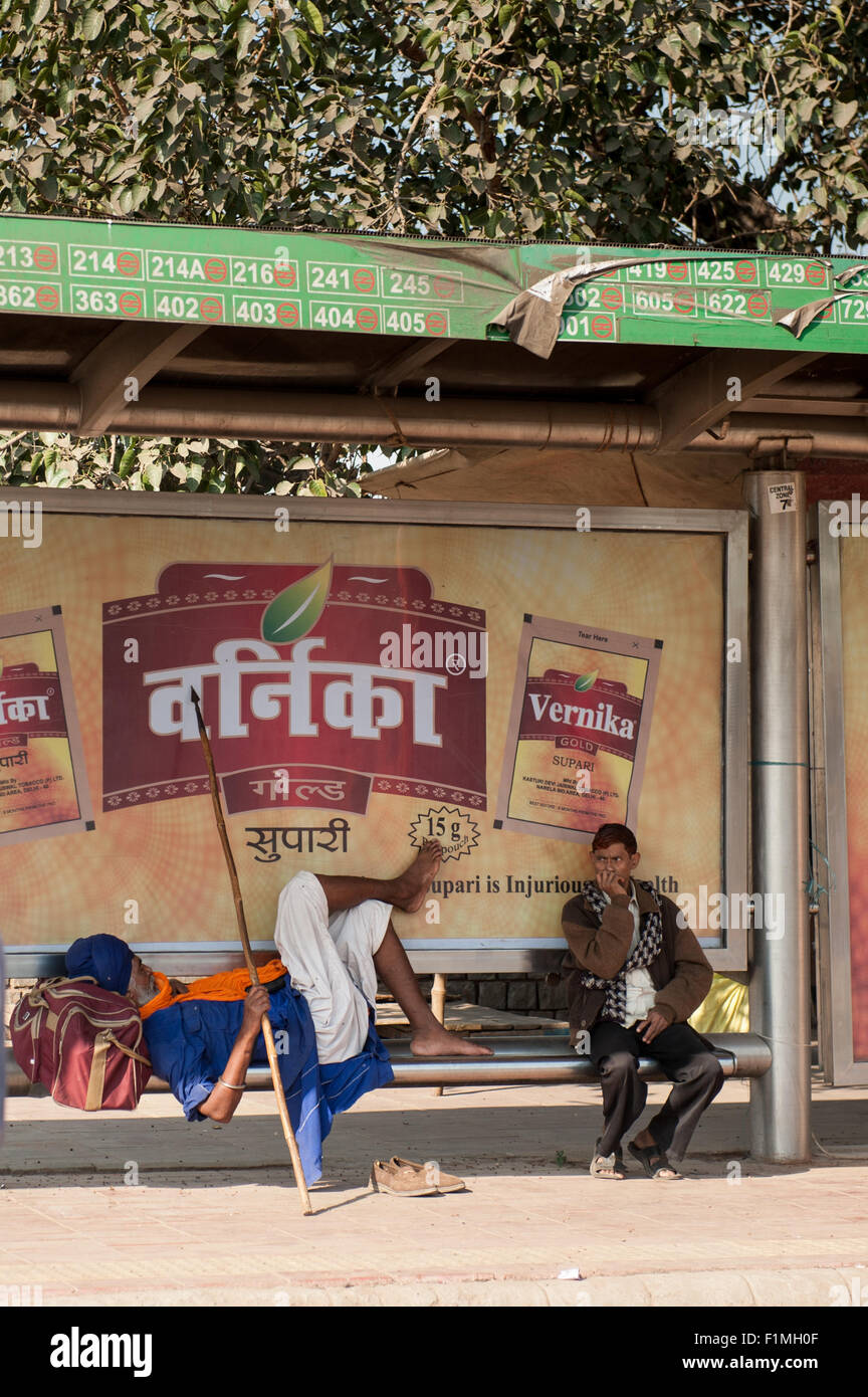 Delhi, India. Sikh Warrior resting at a bus stop with an advertisement for Vernika Gold Supari betel (areca) nut mouth freshener, a non-tobacco carcinogen. The advertisement carries a health warning. Stock Photo