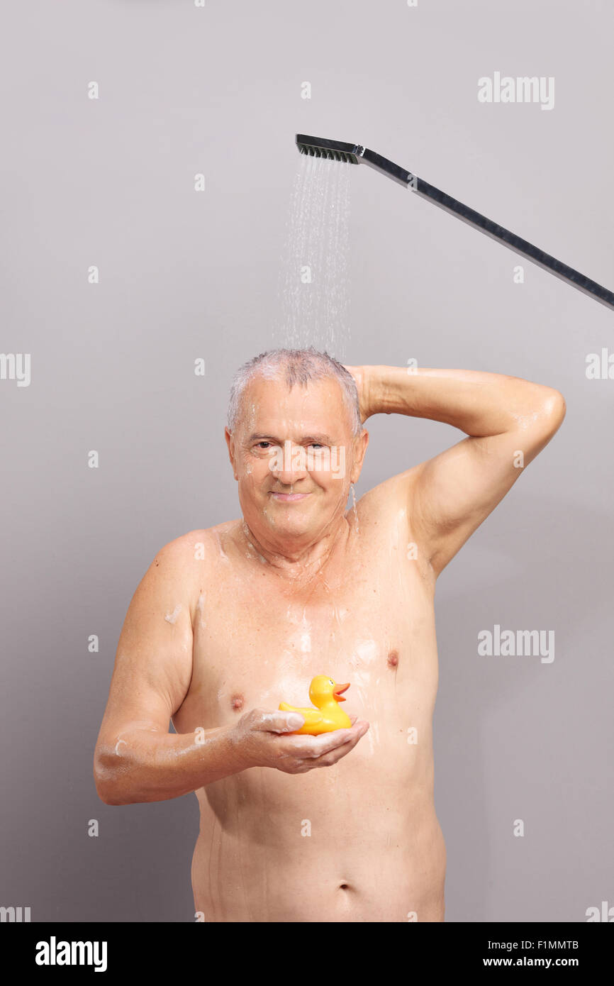 Vertical shot of a senior man taking a shower and holding a yellow rubber duck Stock Photo