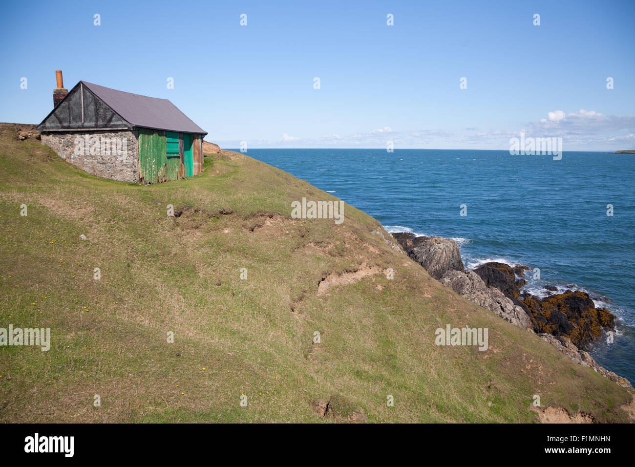 A fishing hut with apex roof and chimney perched on a clifftop above Porth Ysgaden, Tudweiliog, Llyn Peninsula, North Wales Stock Photo
