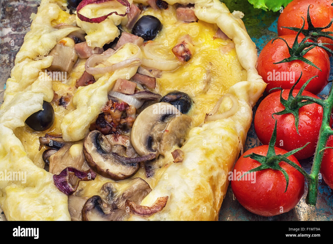 Pizza is of irregular shape elongated in length with fresh vegetables.Tinted Stock Photo