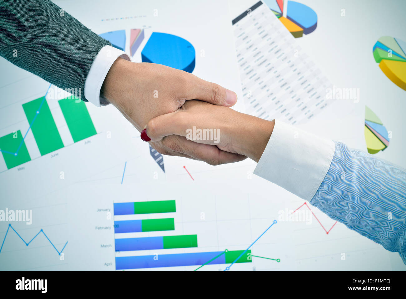 closeup of a businessman and a businesswoman shaking hands above an office desk full of charts Stock Photo