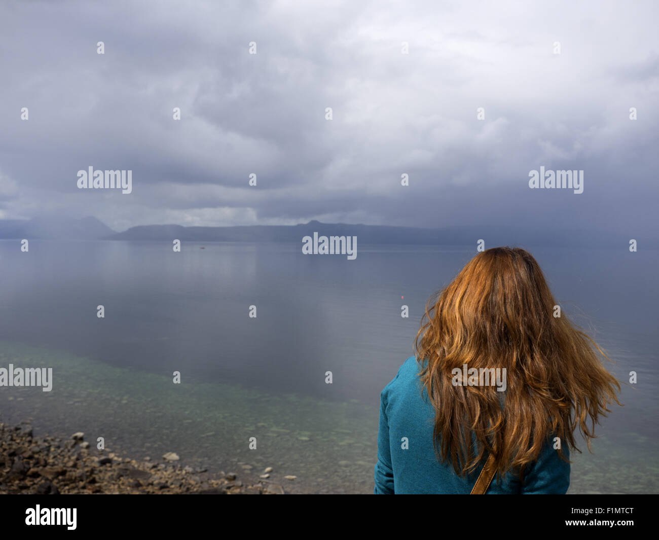 Woman with auburn or chestnut hair looks across to the Isle of Skye from Applecross in Scotland Stock Photo