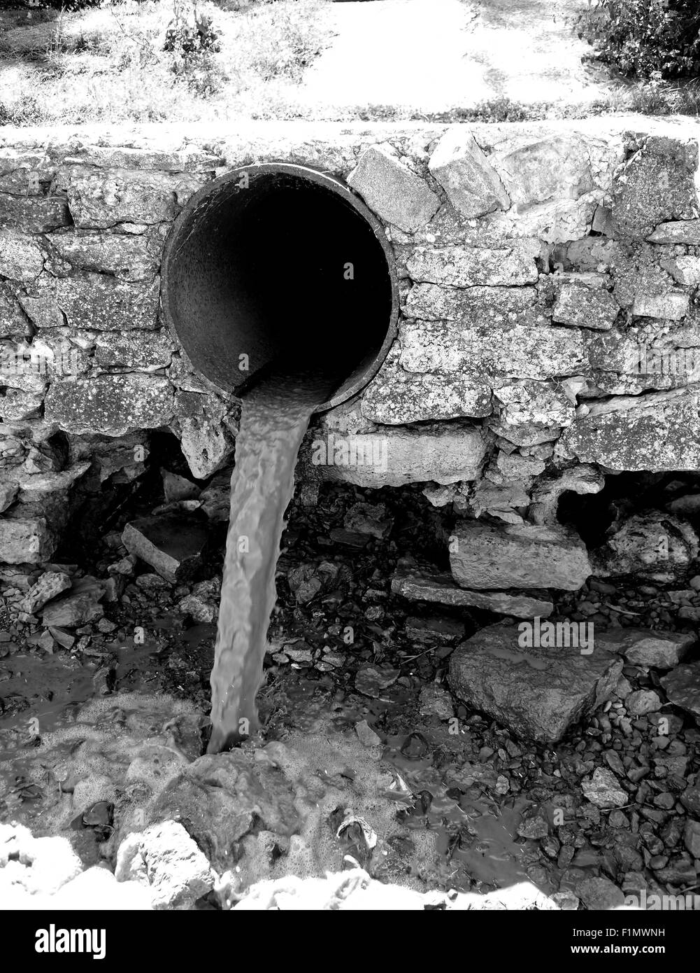 Monochrome view of the dirty water flows from a brown rusty pipes Stock Photo