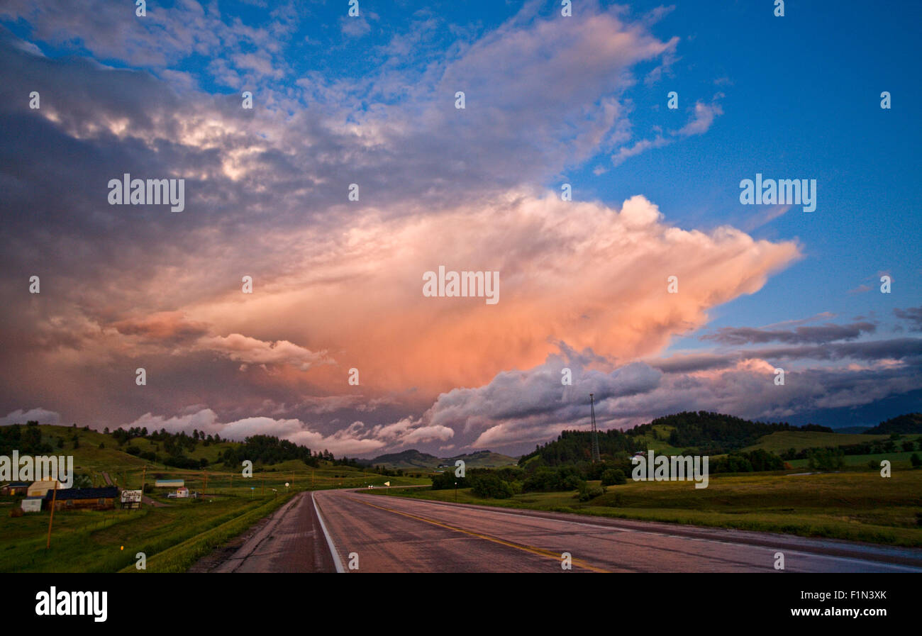 Looking down a empty highway with a pretty sunset on the distant horizon with dark, ominous clouds in the sky Stock Photo