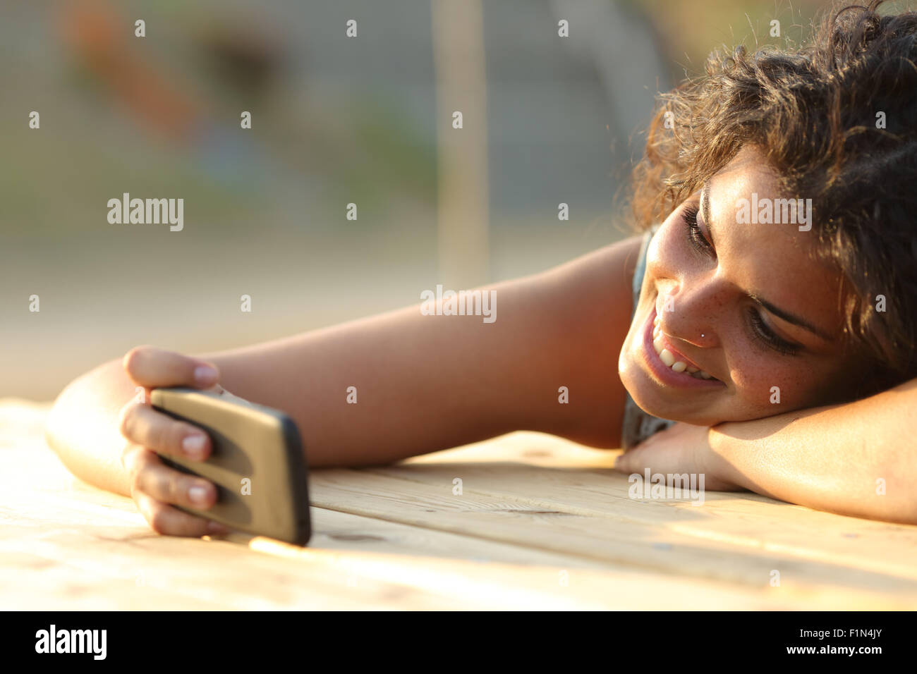 Girl watching videos or social media in a smart phone relaxing in a park at sunset Stock Photo