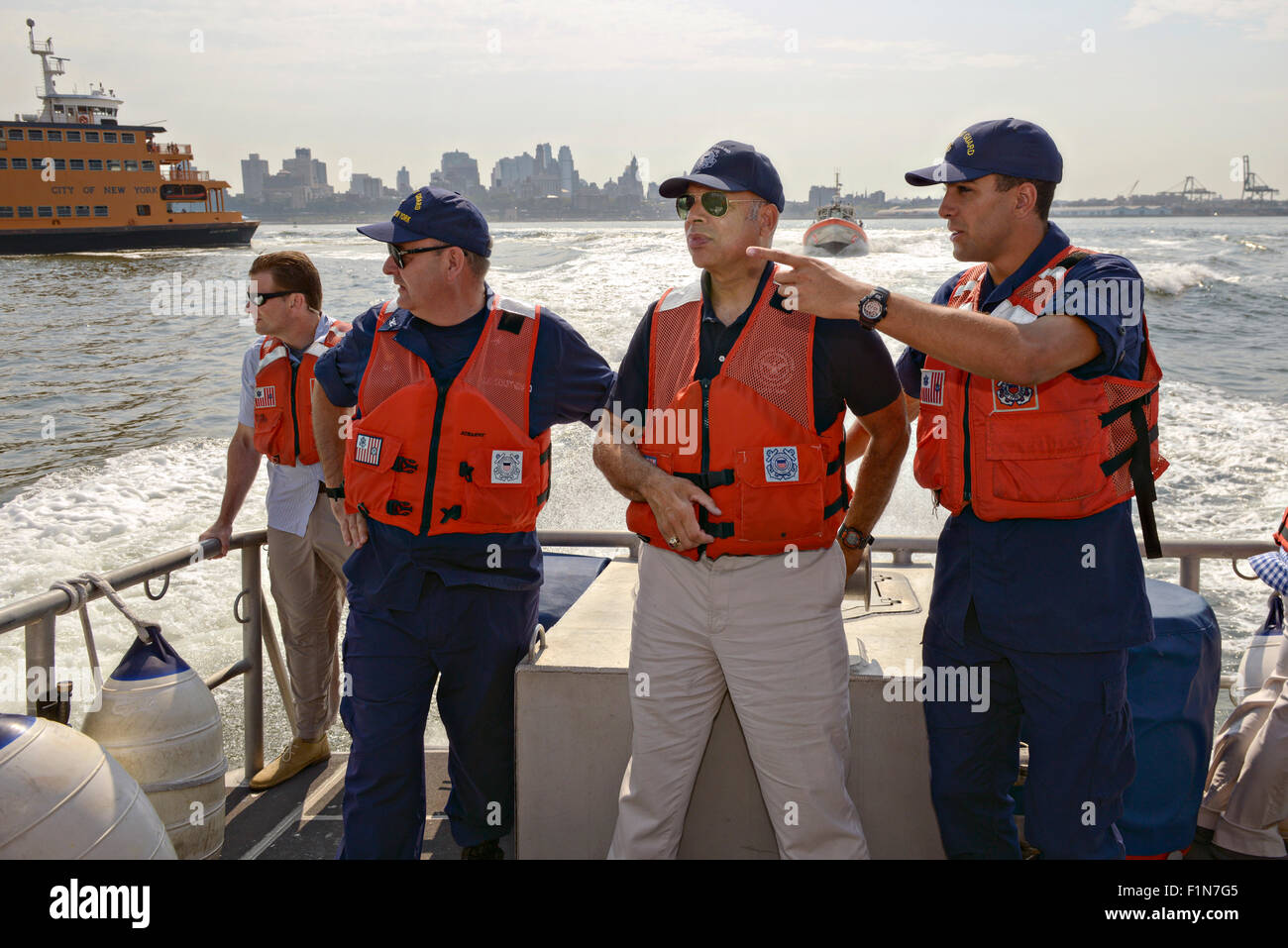 Jeh Johnson Jr., right, talks to his father U.S. Secretary of Homeland Security Jeh Johnson, center, along with Capt. Michael Day, Commander Coast Guard Sector New York, left, during a tour of New York Harbor aboard a Coast Guard 45-foot Response Boat August 18, 2015 in New York City, NY. Stock Photo