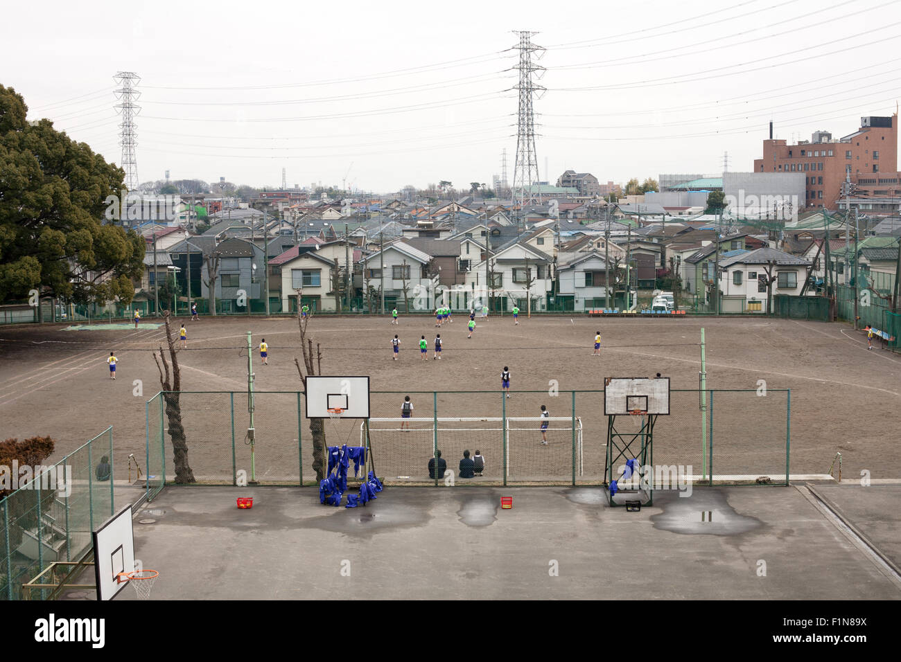 Japanese Junior High School Kids playing in dirt school field with basketball courts in