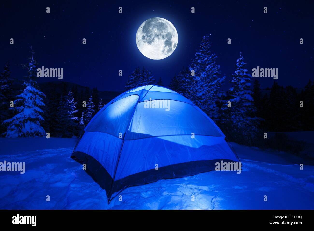 Winter Night Camping in Heavy Mountains Snow. Large Full Moon on the NIght Sky. Outdoor and Recreation Theme. Stock Photo