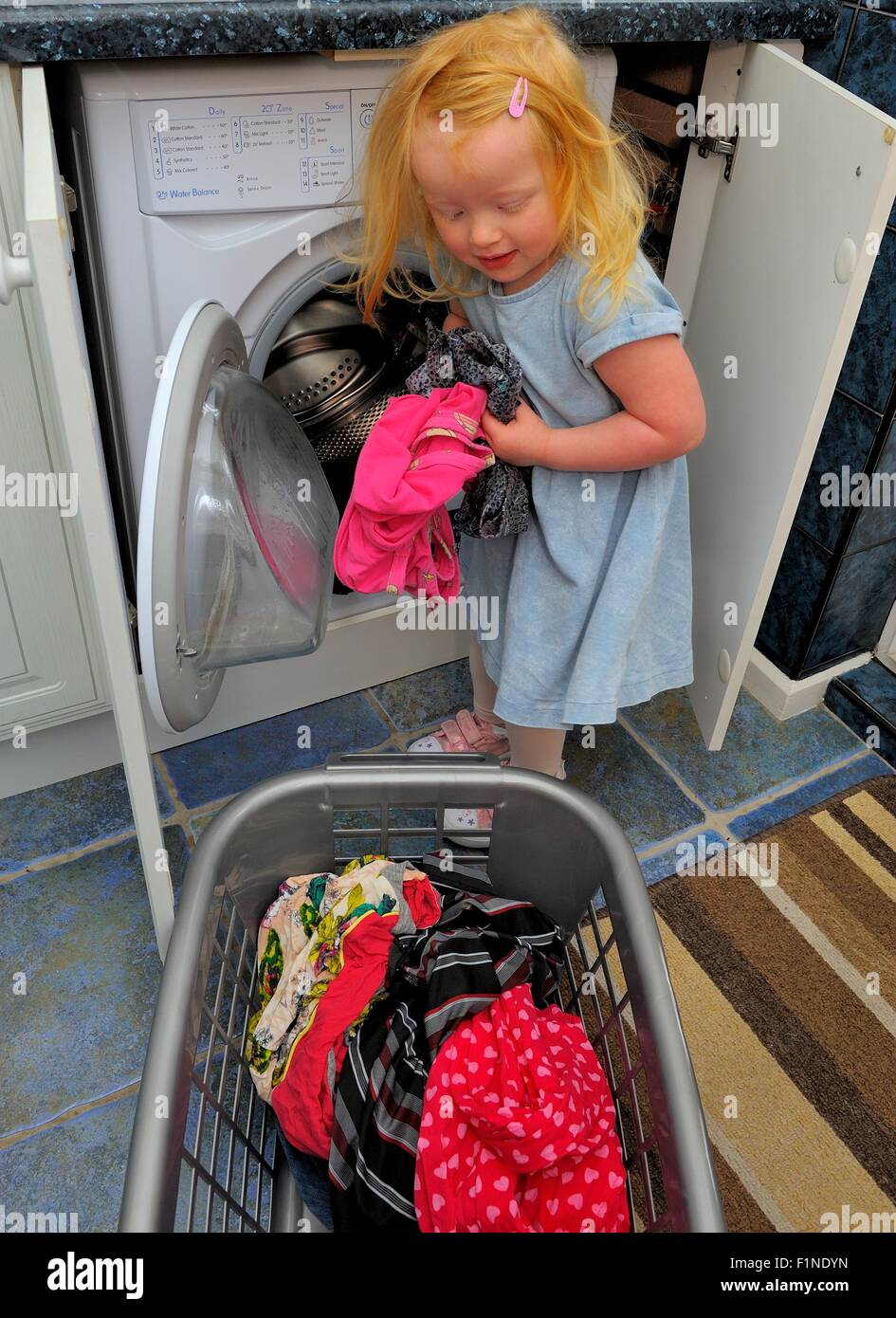 A 3 year old girl removing washing from a washing machine and loading it into a laundry basket. Stock Photo