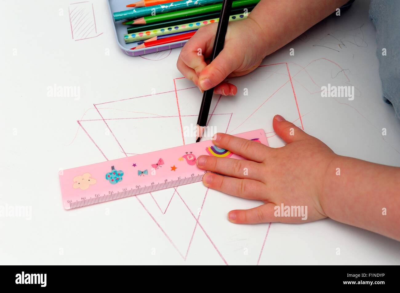 A 3 year old toddler girl using a ruler to draw straight lines Stock Photo