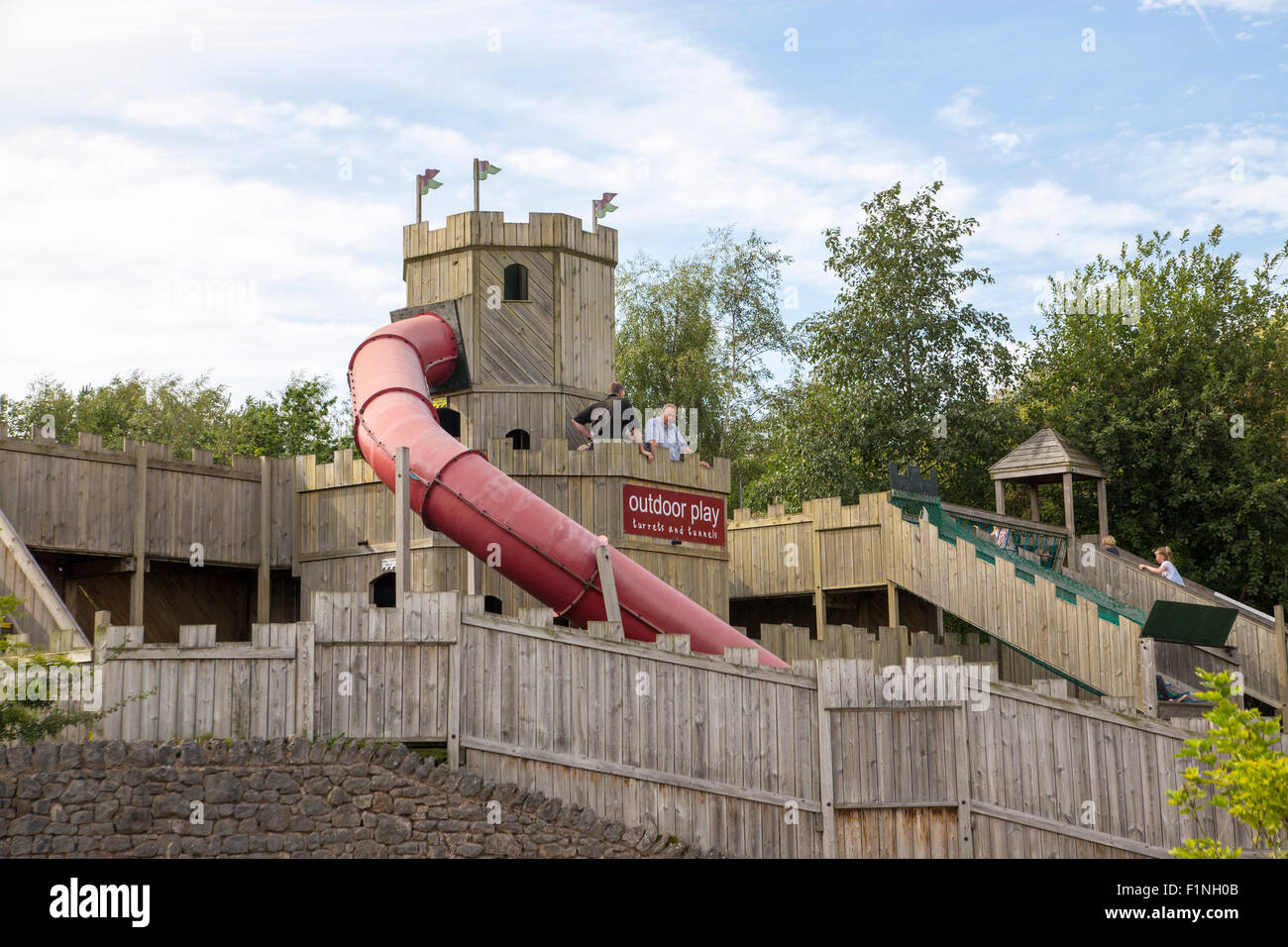 Large wooden outdoor adventure playground.  Castle themed playground with slides, climbing wall and swings Stock Photo