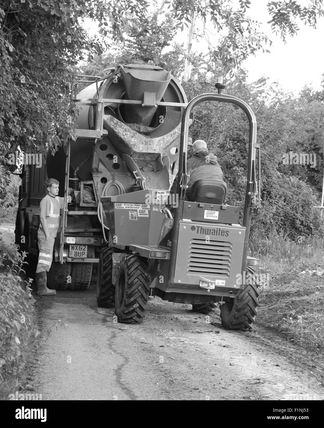 Unloading a concrete truck in a narrow country lane into a small builders dump truck for placing on a farm Stock Photo