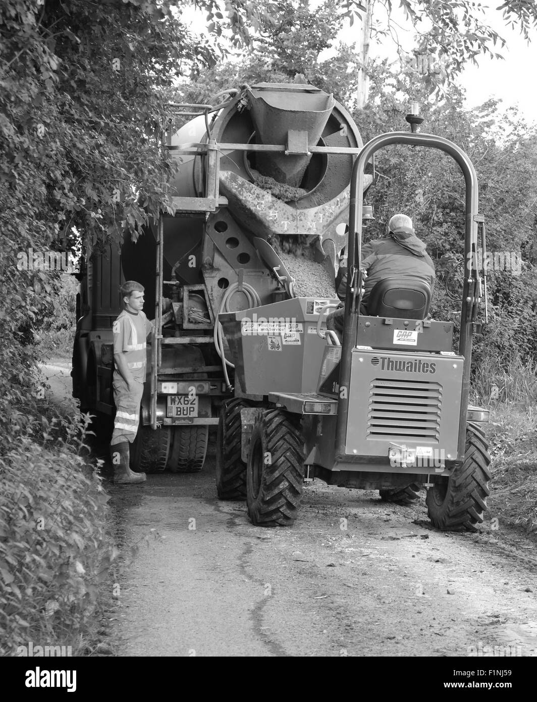 Unloading a concrete truck in a narrow country lane into a small builders dump truck for placing on a farm Stock Photo