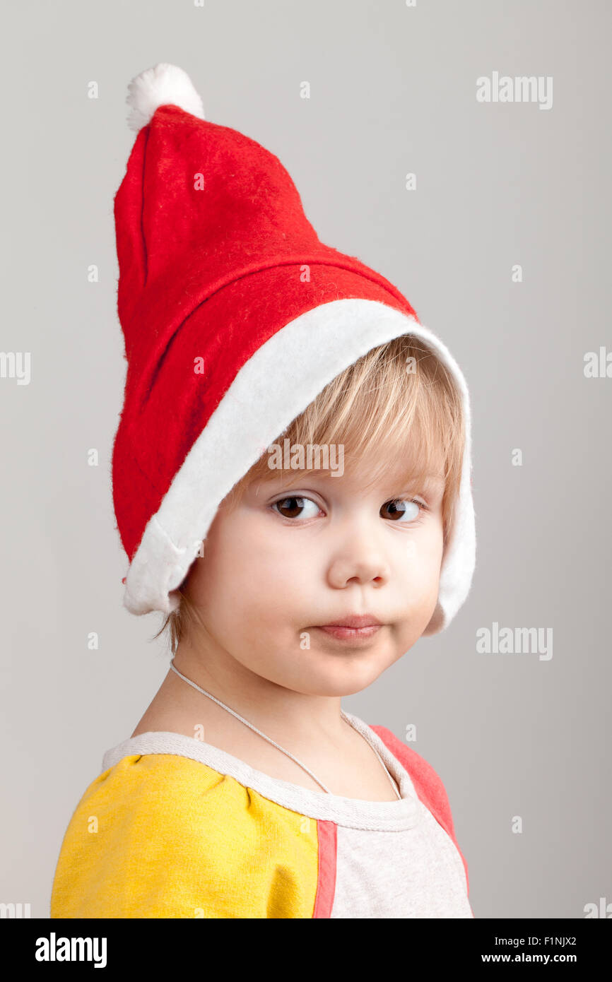 Cute Caucasian little girl in red Santa hat on gray background, closeup studio portrait Stock Photo