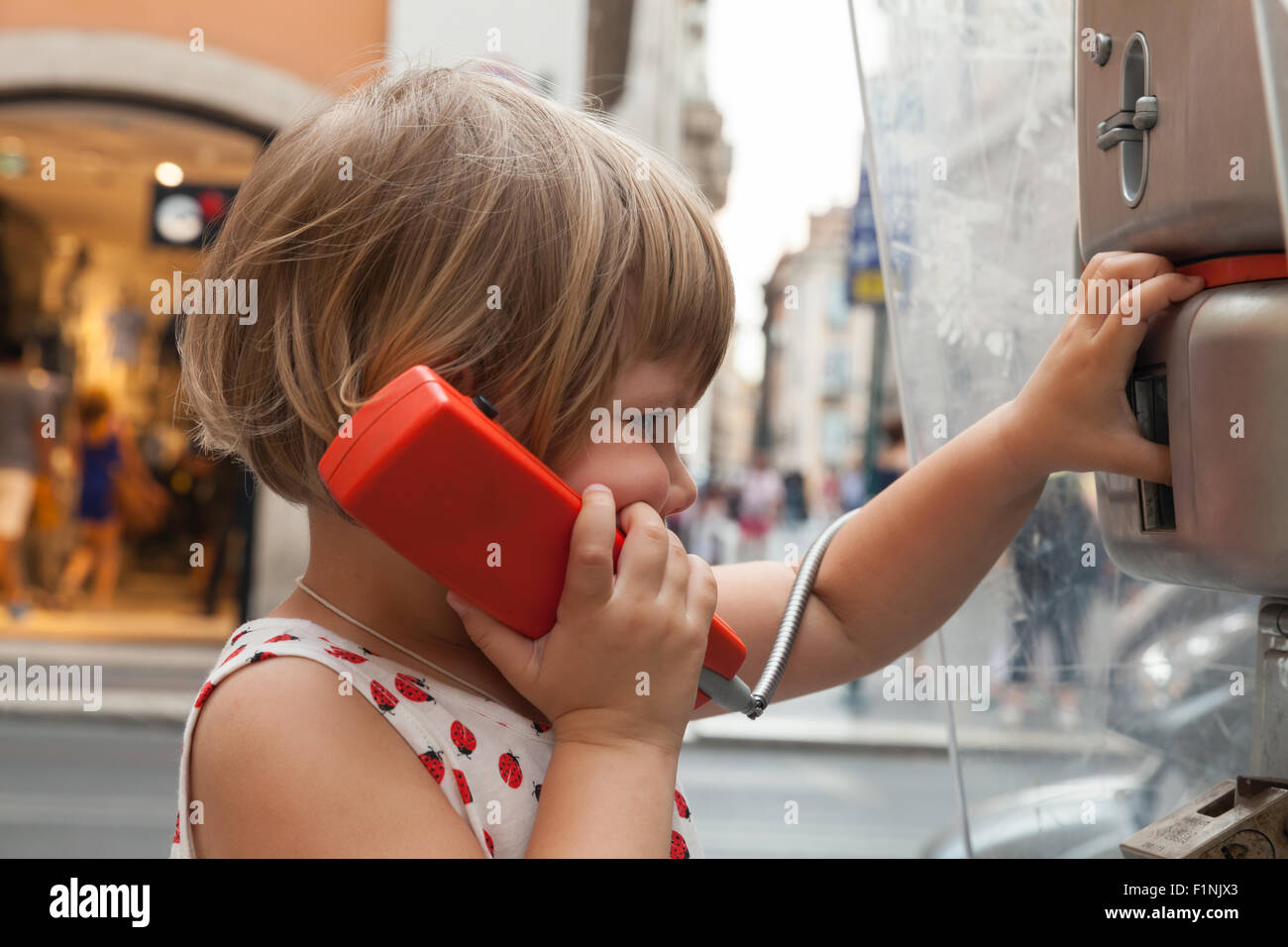 Outdoor portrait of little blond girl talking on the urban street phone Stock Photo