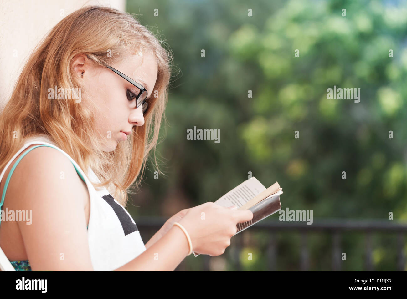 Blond Caucasian teenage girl sits on the balcony and read a book Stock Photo