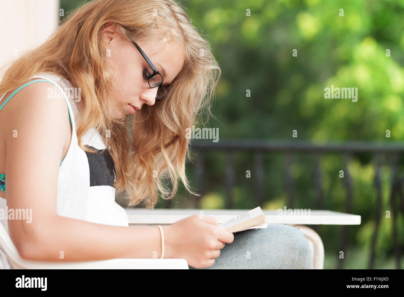 Blonde Caucasian teenage girl sits on the balcony and read a book Stock Photo