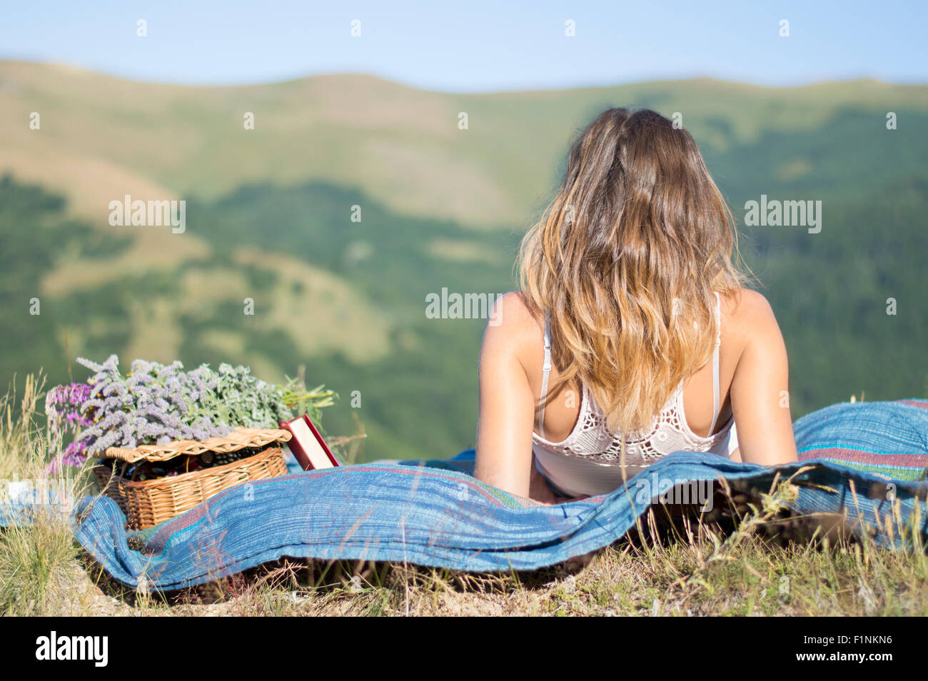 Girl laying on a blanket on a picnic in the field facing the view at the mountains Stock Photo