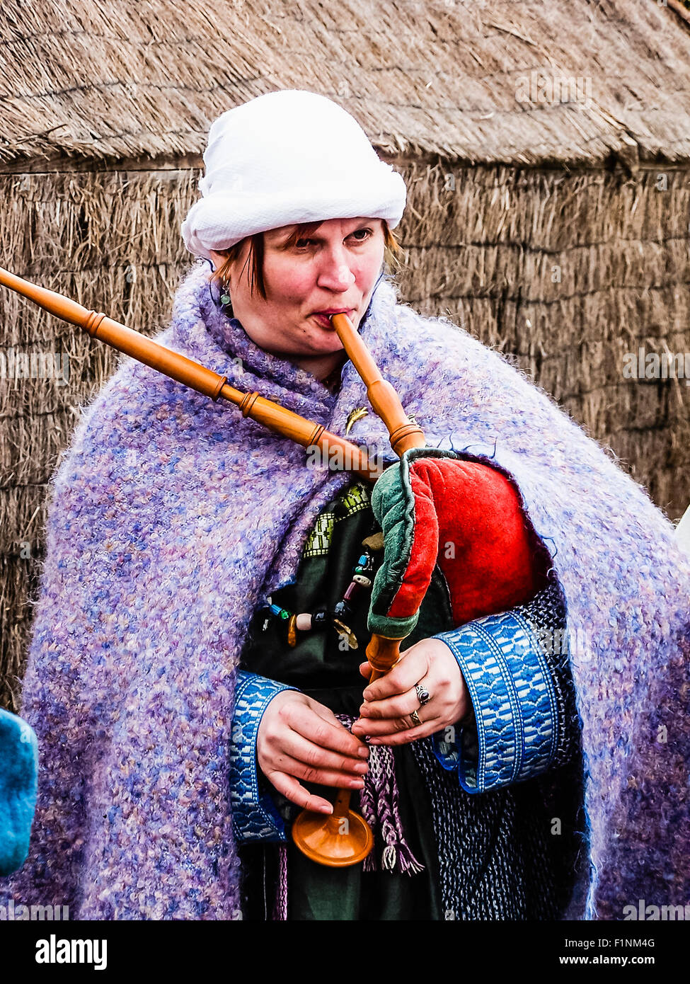 A woman dressed in medieval clothing plays a traditional set of bagpipes. Stock Photo