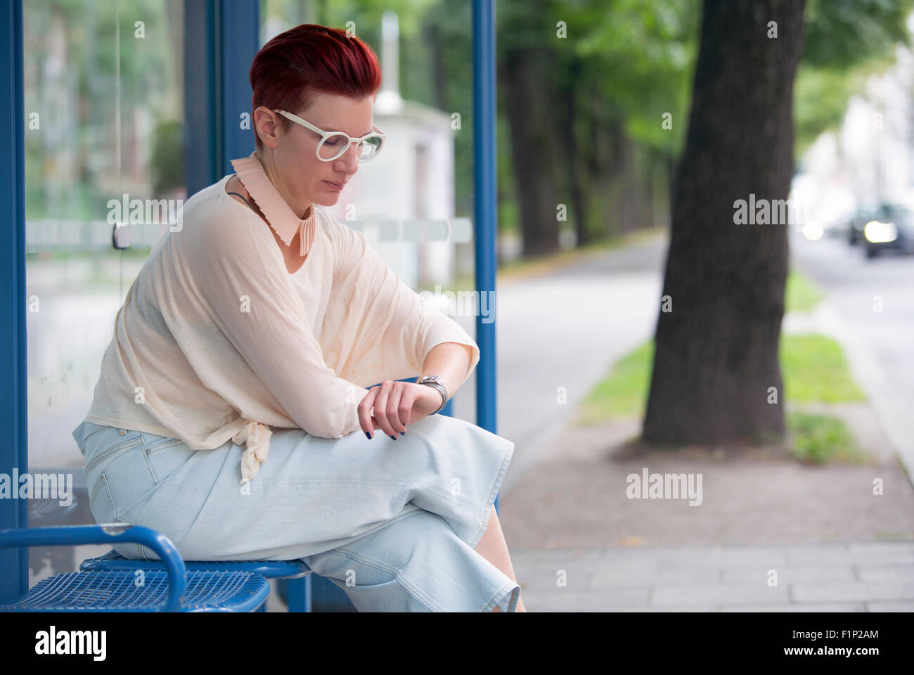 red-haired woman sitting at bus stop and looking at her watch Stock Photo