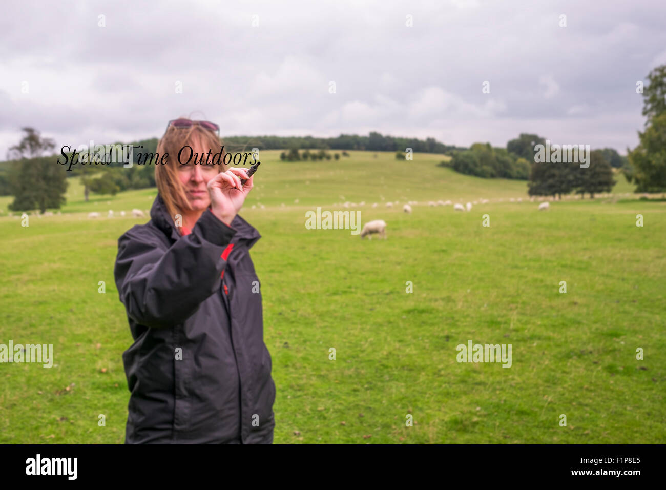 A middle aged woman outside in the southdowns national park writing on the words  ' spend time outside  'on a invisible screen Stock Photo