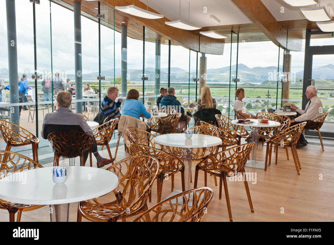 Visitors relax in the cafe within the Harlech Castle visitor center, with a vista of Snowdonia through giant windows Stock Photo