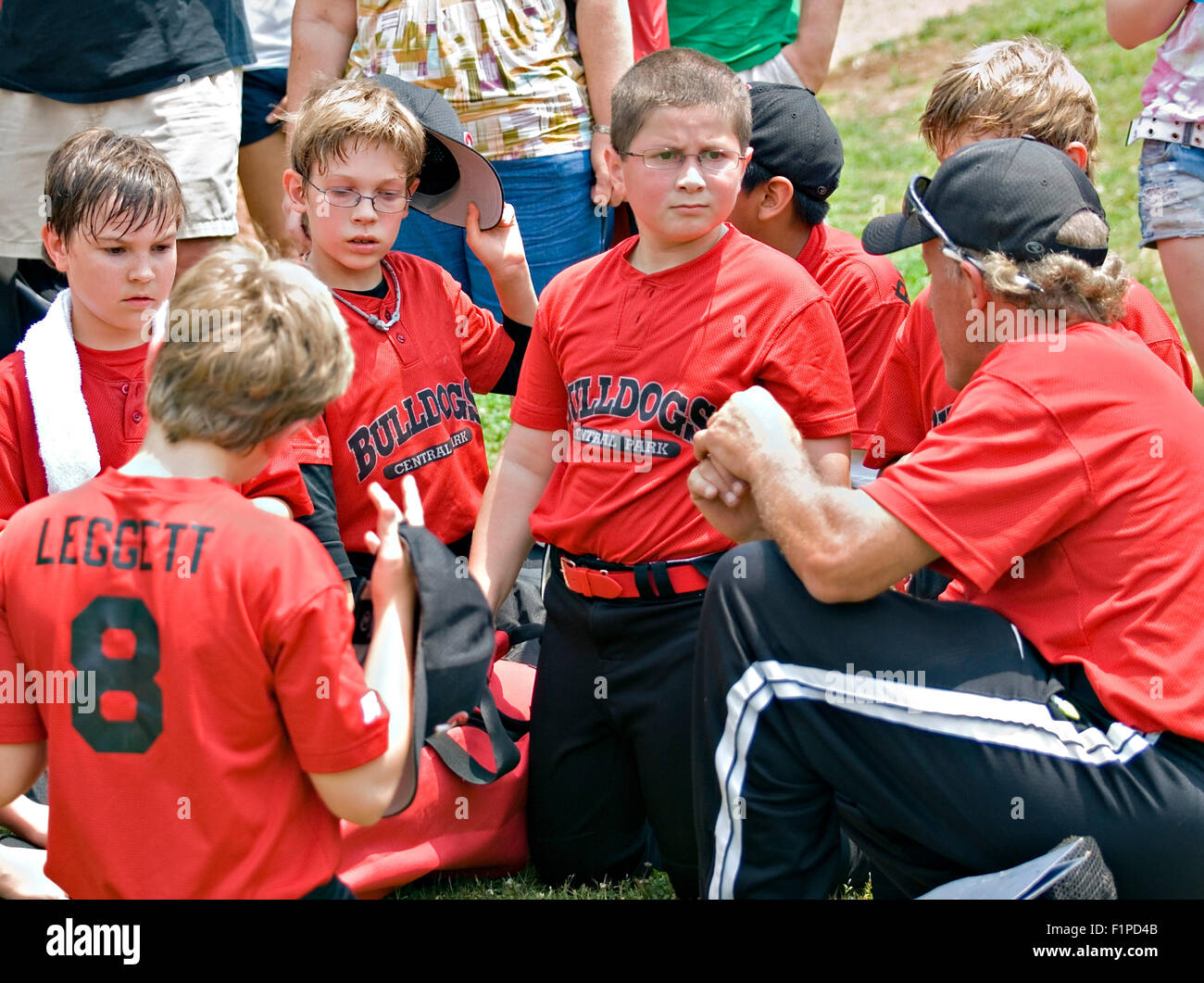 A coach talking to his little league baseball team, families are in the background listening. Stock Photo