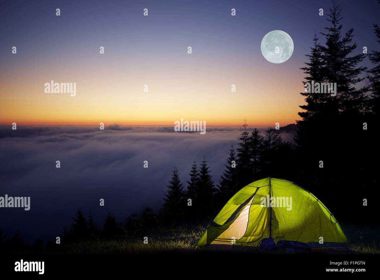 Tent Camping in a Forest During Full Moon Night. Foggy Mountains Camping. Stock Photo