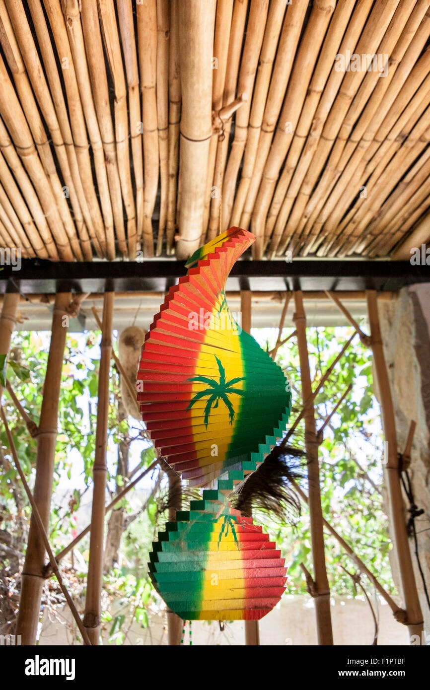 Hanging wooden spiral decorative craft with reggae color over open window of a tropical hut Stock Photo