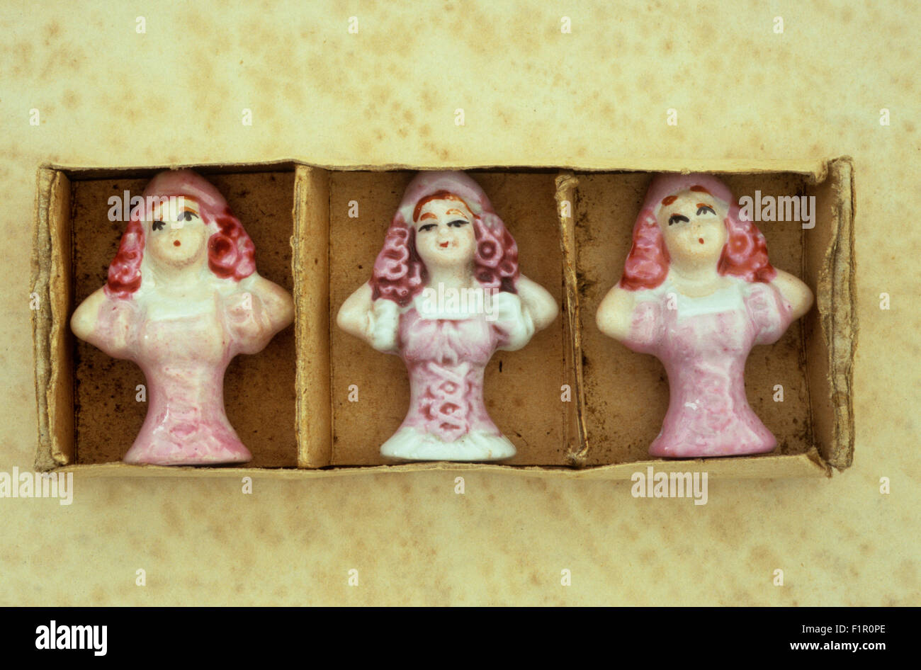 Three porcelain half-dolls from pin-cushions in pink bodices identical but painted differently in cardboard box Stock Photo