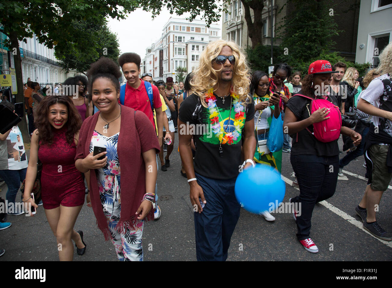 Man wearing a blonde wig. Notting Hill Carnival in West London. A celebration of West Indian / Caribbean culture and Europe's largest street party, festival and parade. Revellers come in their hundreds of thousands to have fun, dance, drink and let go in the brilliant atmosphere. It is led by members of the West Indian / Caribbrean community, particularly the Trinidadian and Tobagonian British population, many of whom have lived in the area since the 1950s. The carnival has attracted up to 2 million people in the past and centres around a parade of floats, dancers and sound systems. Stock Photo