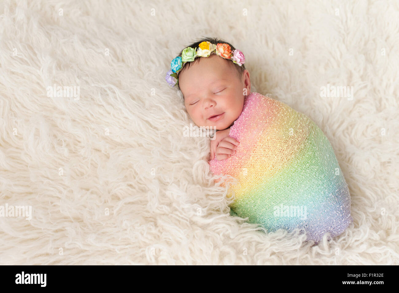 Smiling Newborn Baby Girl Wrapped in a Rainbow Colored Swaddle Stock