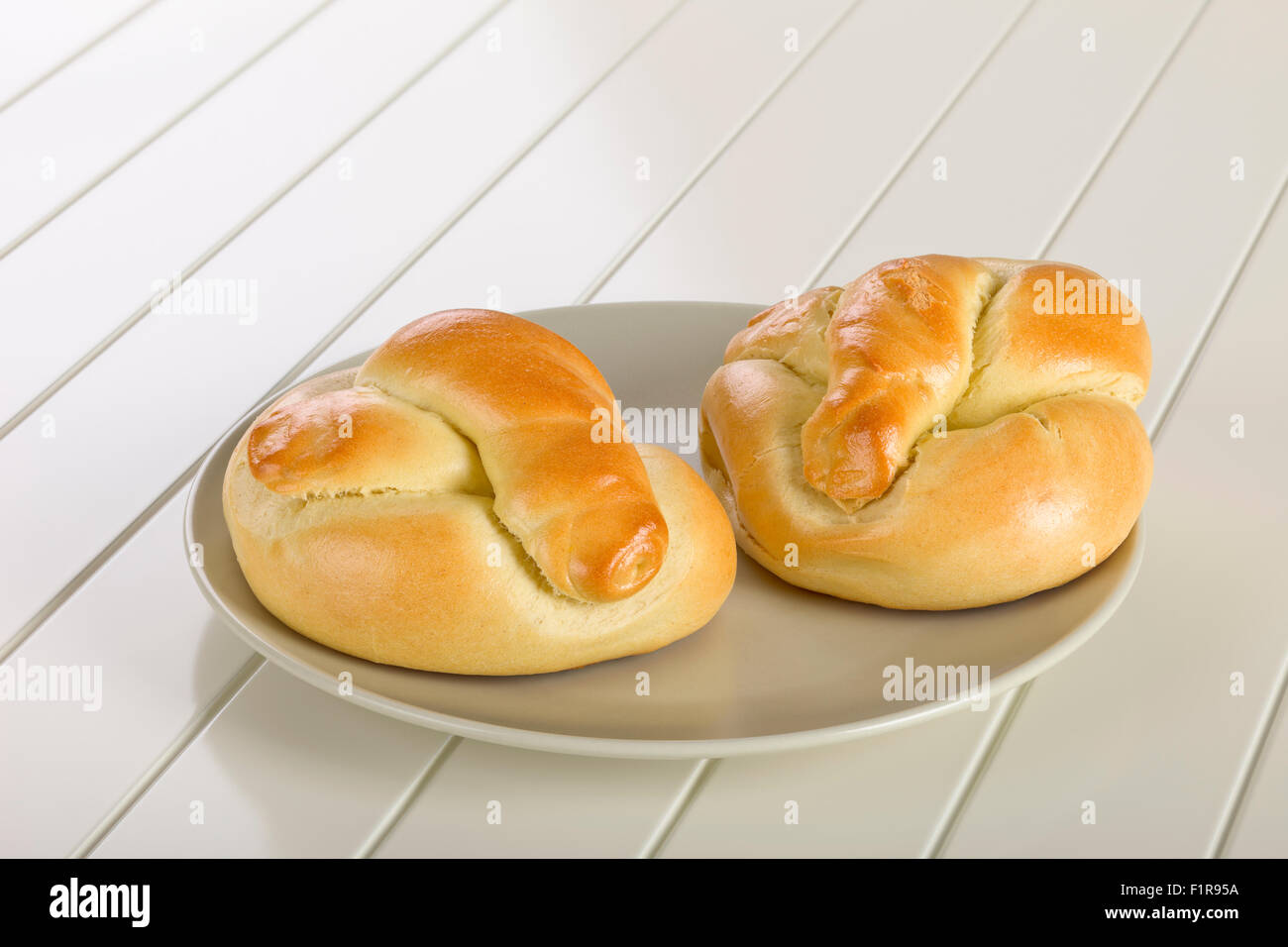Bread roll on ceramic plate, white wooden background. Stock Photo