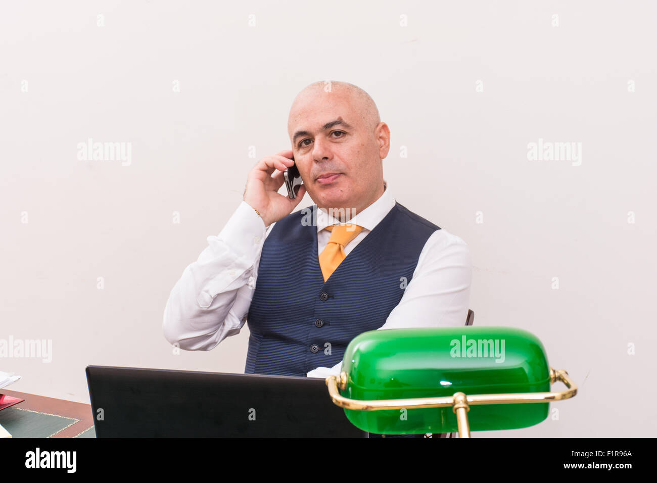 A business man on the phone and pc, at desk, in conference call and bald. An antique desk and important. Stock Photo